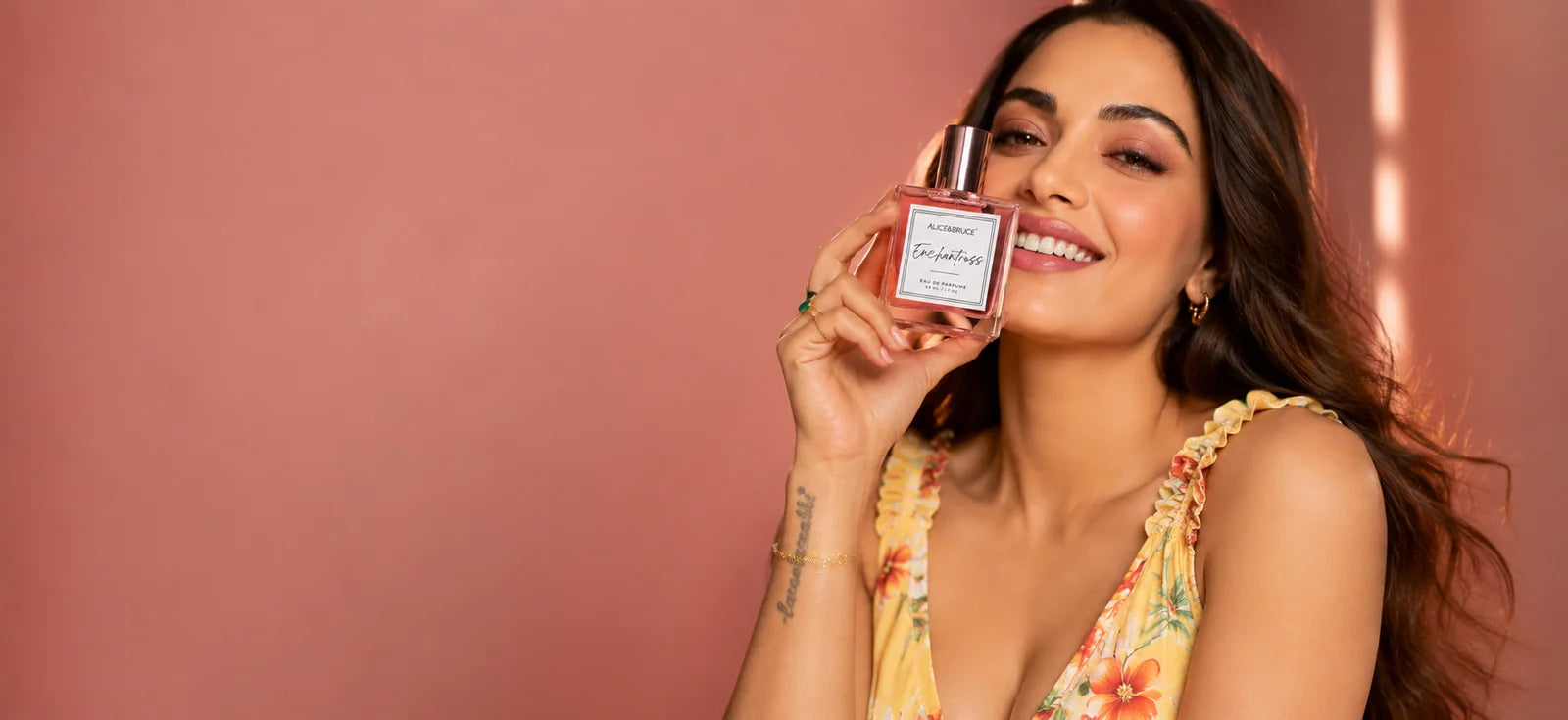 Woman smiling while holding Alice and Bruce Enchantress luxury perfume against a soft pink background